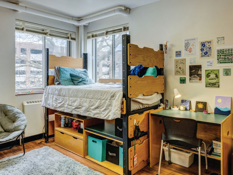 A college dorm room with two beds, a chair, and decorative orange leaves on the wall.